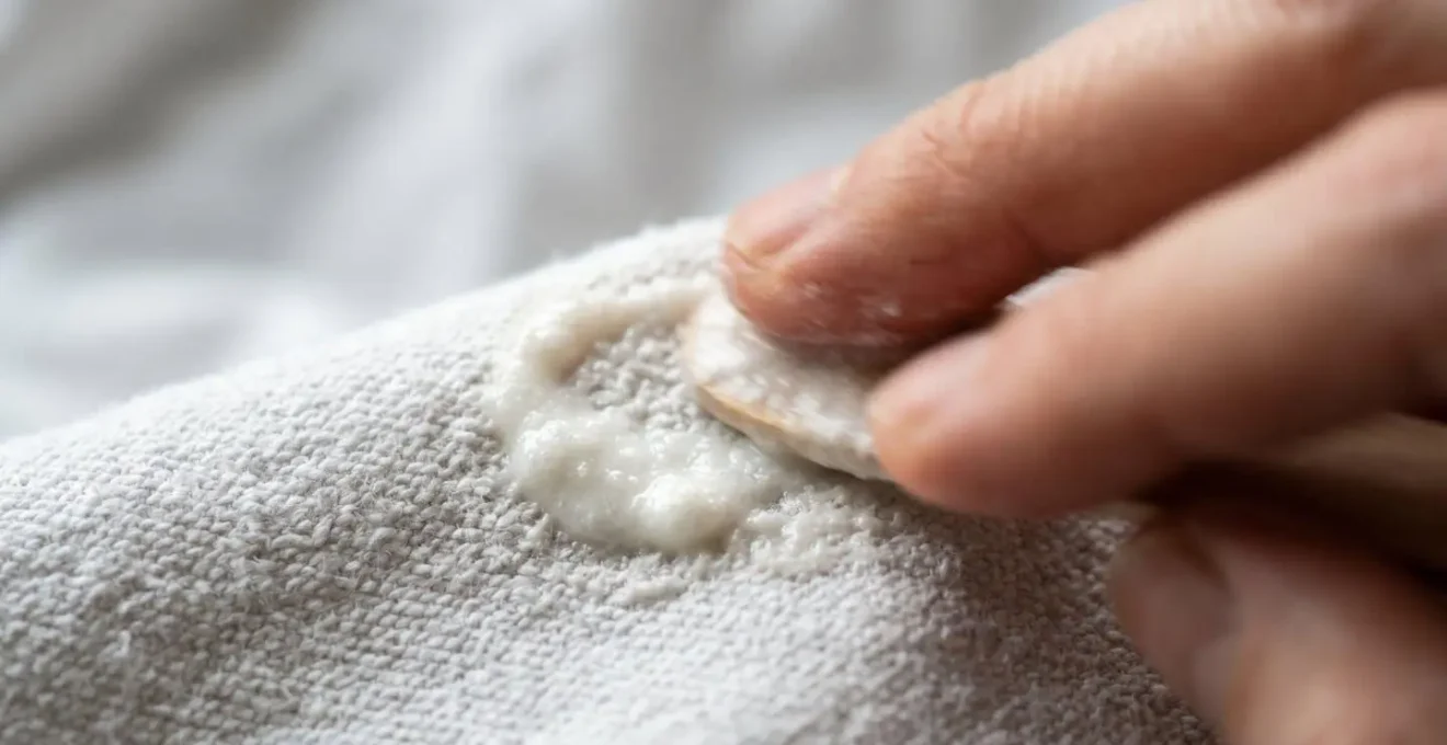 Manos aplicando pasta blanqueadora casera sobre manchas de camisa blanca