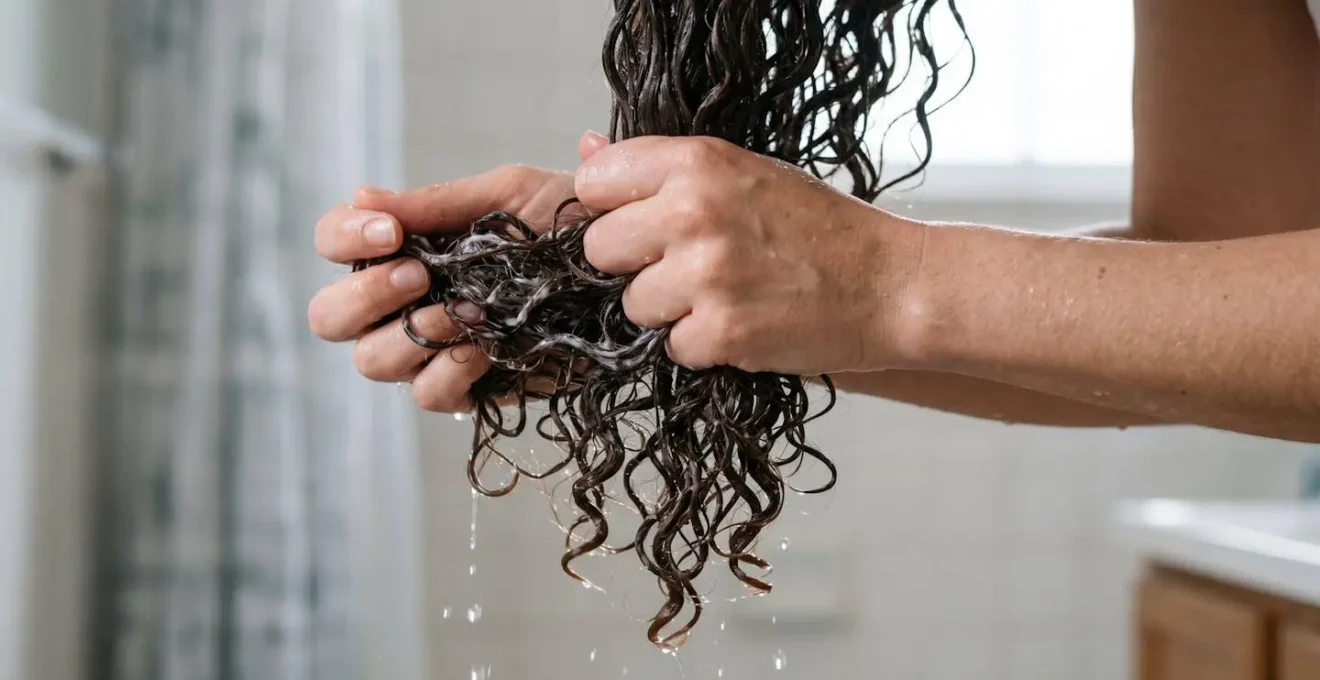 Manos aplicando técnica de estrujado con agua y acondicionador en mechones de pelo