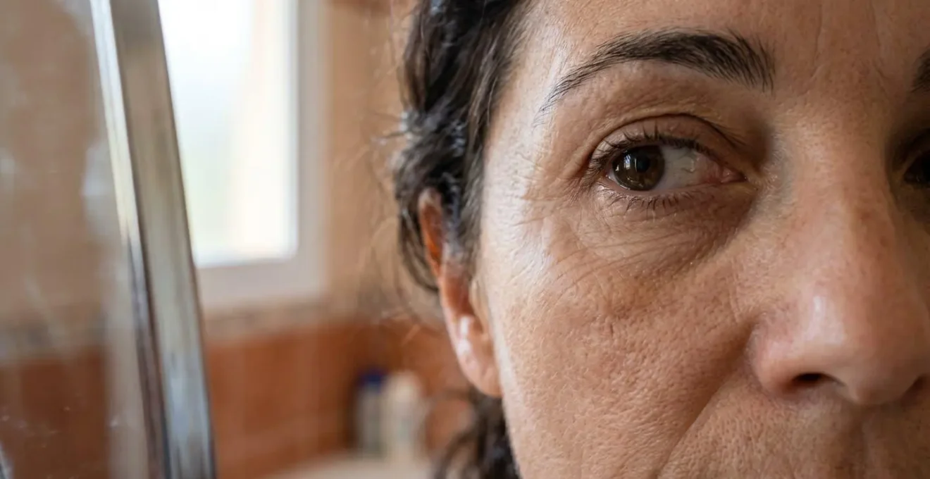 Primer plano de rostro femenino examinando líneas de expresión matutinas en espejo del baño